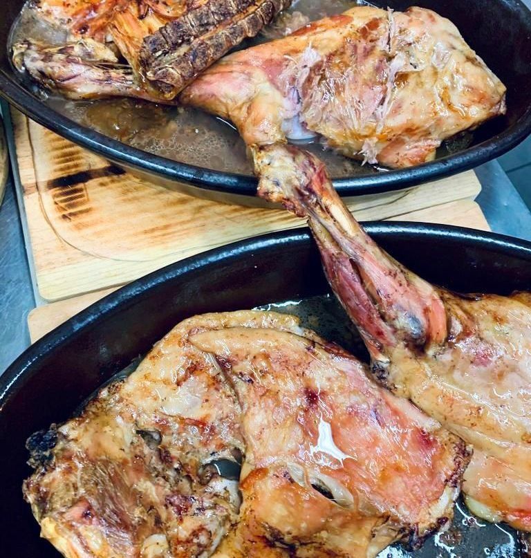 Pierna de cordero asada en sartén negra, con la piel dorada y el hueso visible.