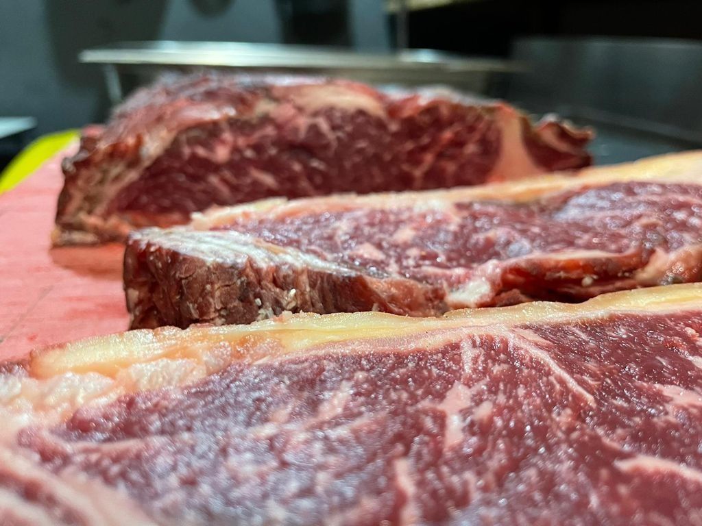 Primer plano de tres filetes crudos y rojos con marmoleado sobre una tabla de cortar.