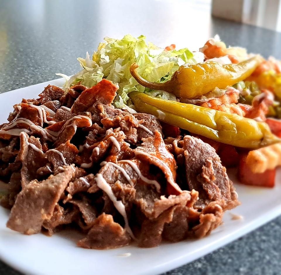 Doner kebab salaatin, paprikoiden ja kastikkeen kera valkoisella lautasella.