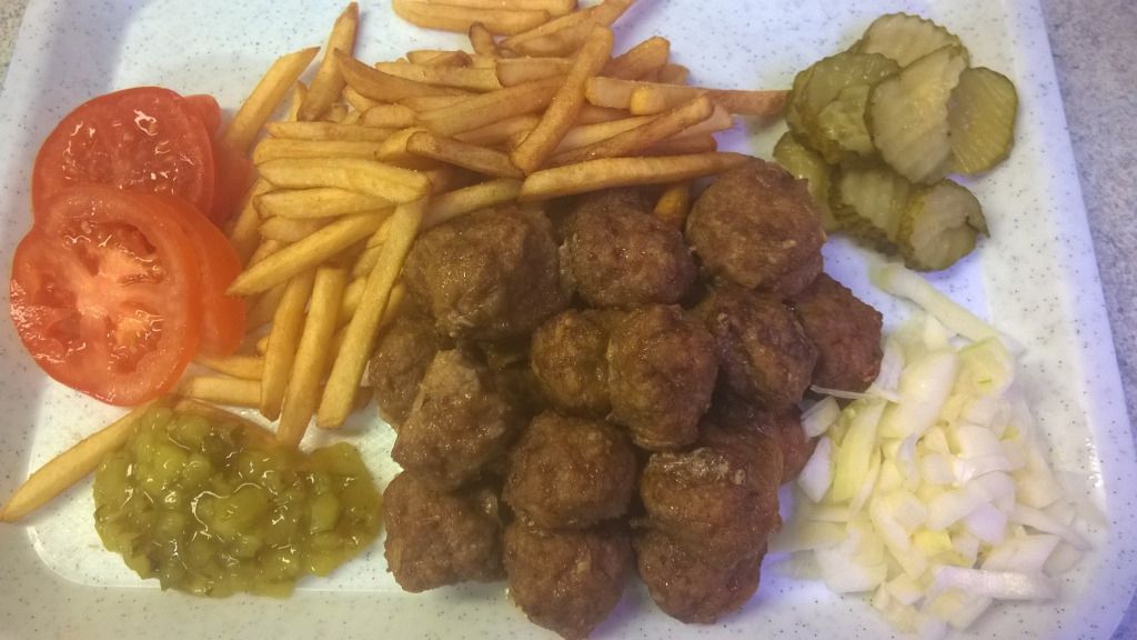 Lautanen, jossa on lihapullia, ranskalaisia, tomaatteja, suolakurkkuja, sipulia ja relish-kastiketta.