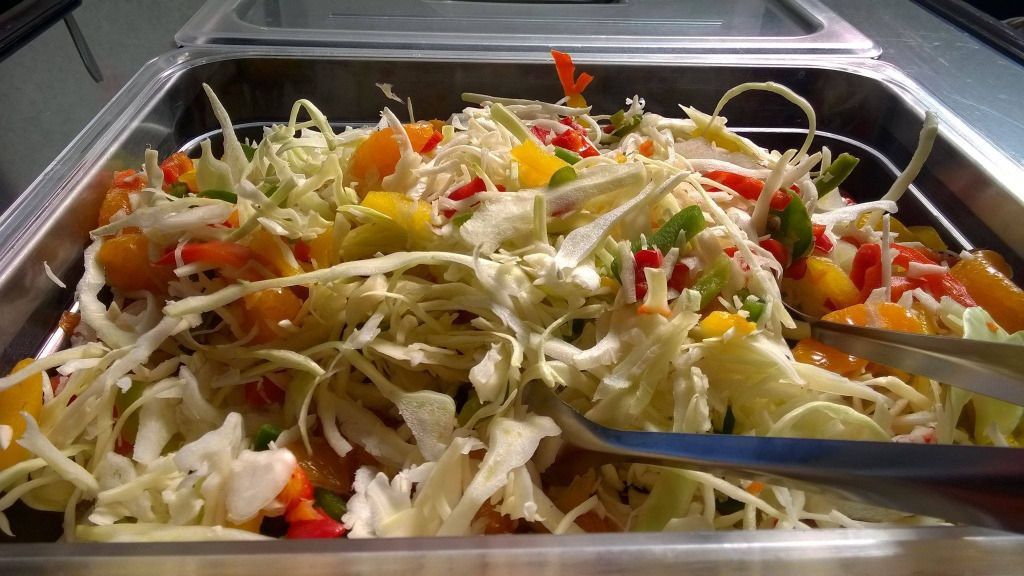 Salaattipöytä, jossa on silputtua kaalia, keltaisia ​​ja punaisia ​​paprikoita sekä tarjoilupihdit.