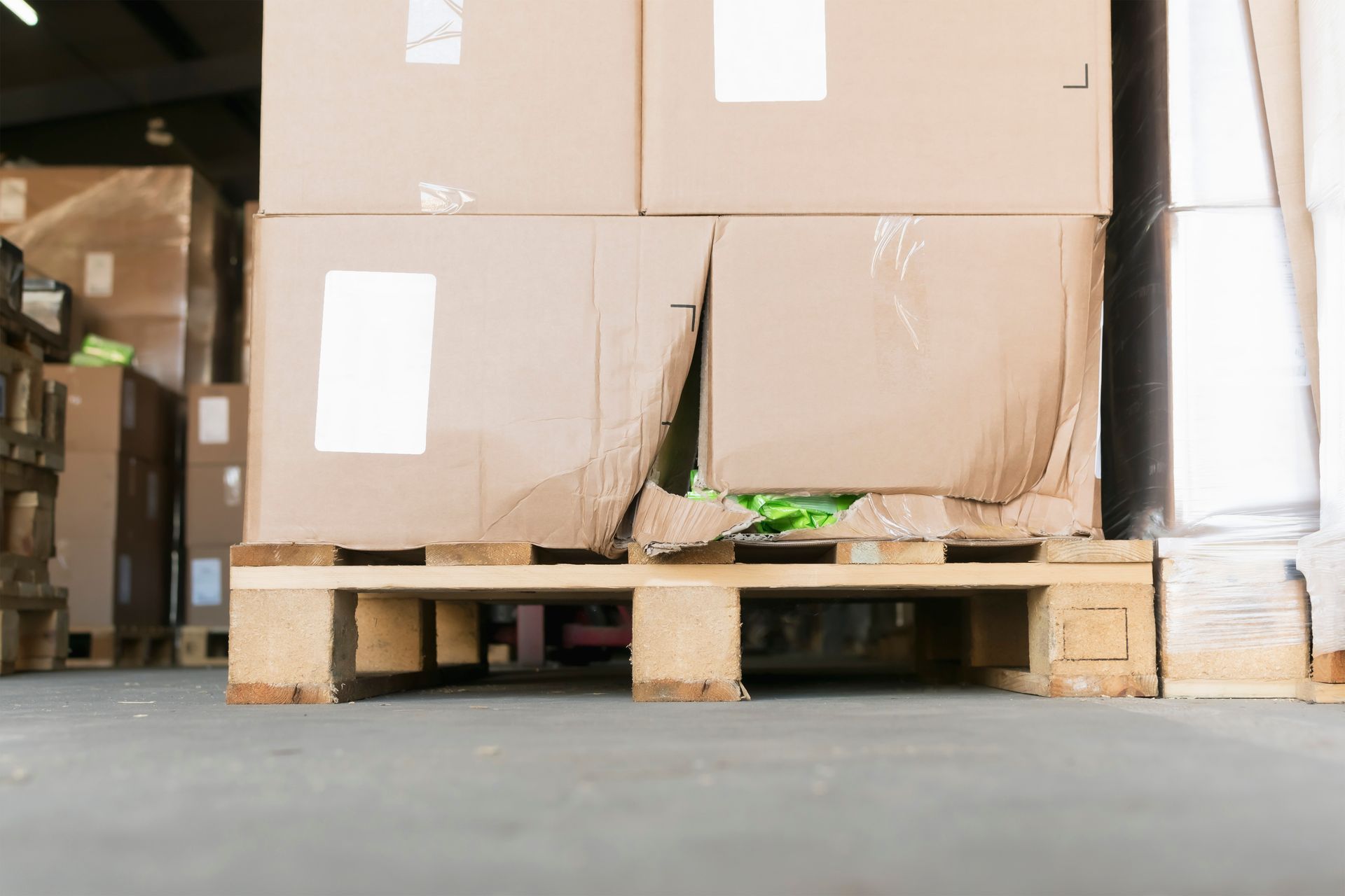 Des cartons endommagés sont empilés sur une palette d'expédition en bois dans un entrepôt.