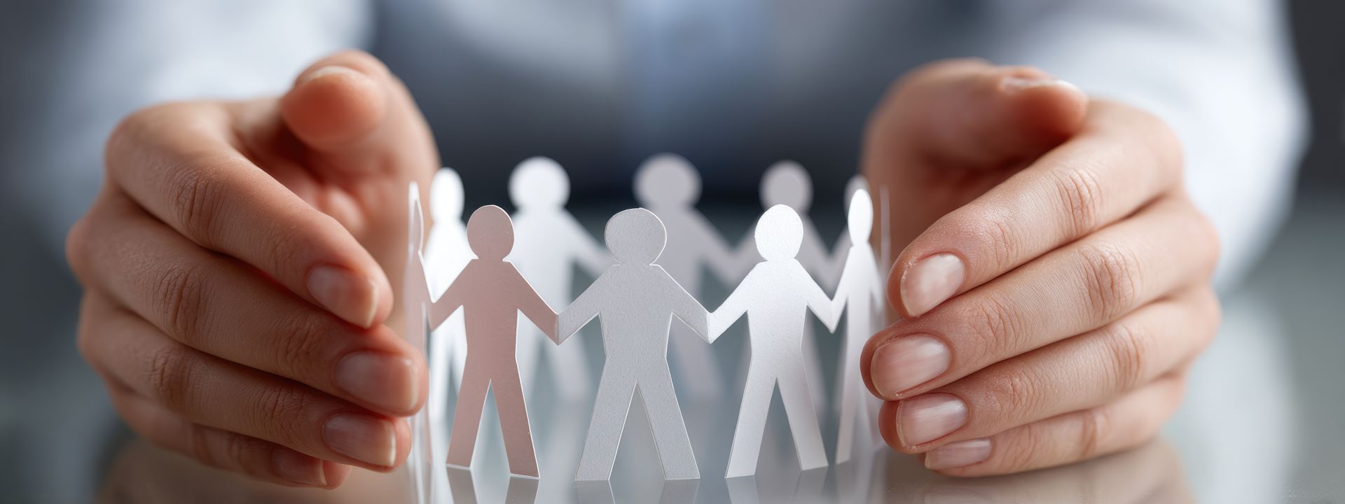 Des mains enserrent délicatement une silhouette circulaire en papier blanc, se tenant la main, posée sur un bureau.
