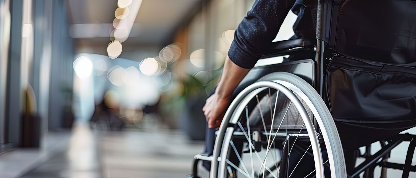 Une personne est assise dans un fauteuil roulant dans un couloir lumineux, sur un fond flou.