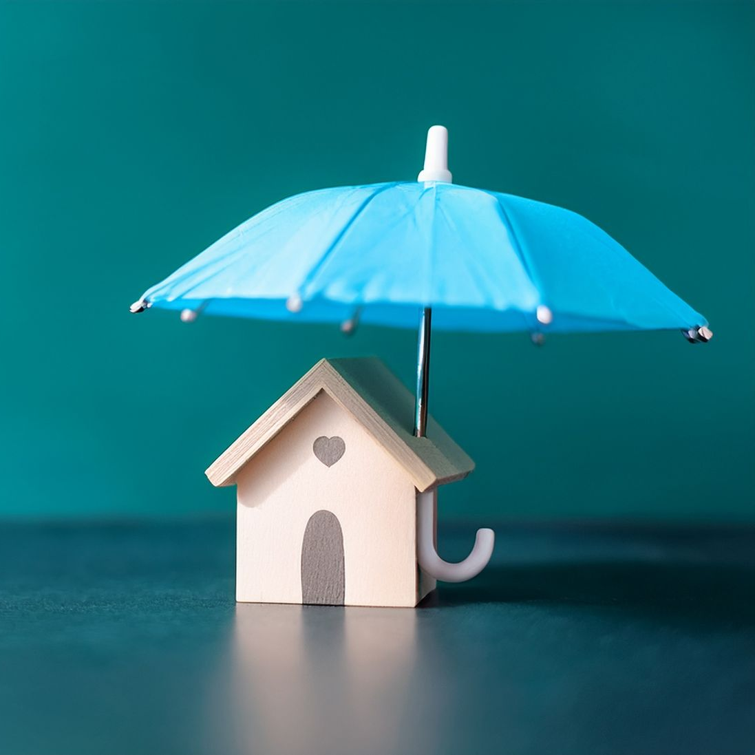 Une petite maison miniature est placée sous un minuscule parasol bleu sur un fond bleu sarcelle foncé.