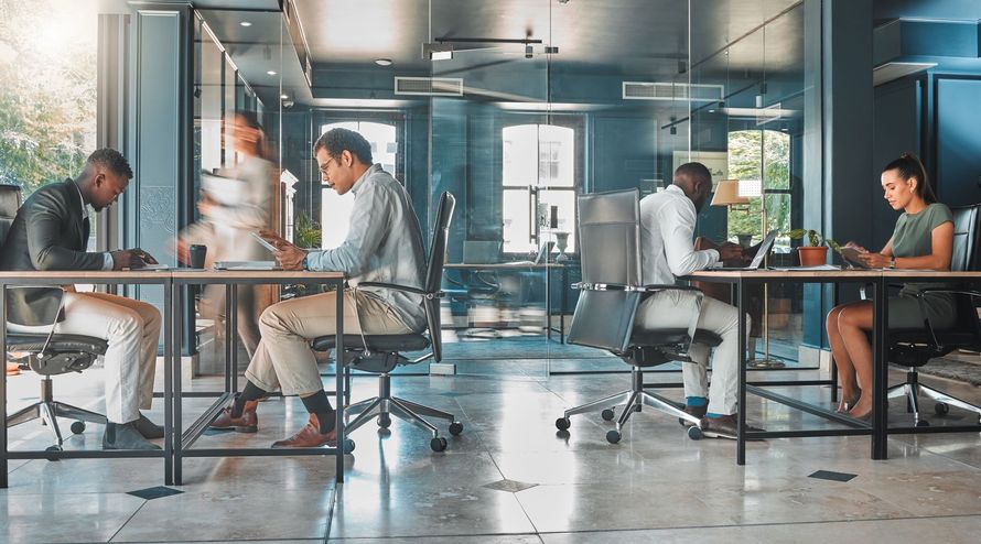Des professionnels travaillent à des bureaux dans un espace de travail moderne et ouvert, avec des cloisons vitrées et de la lumière naturelle.