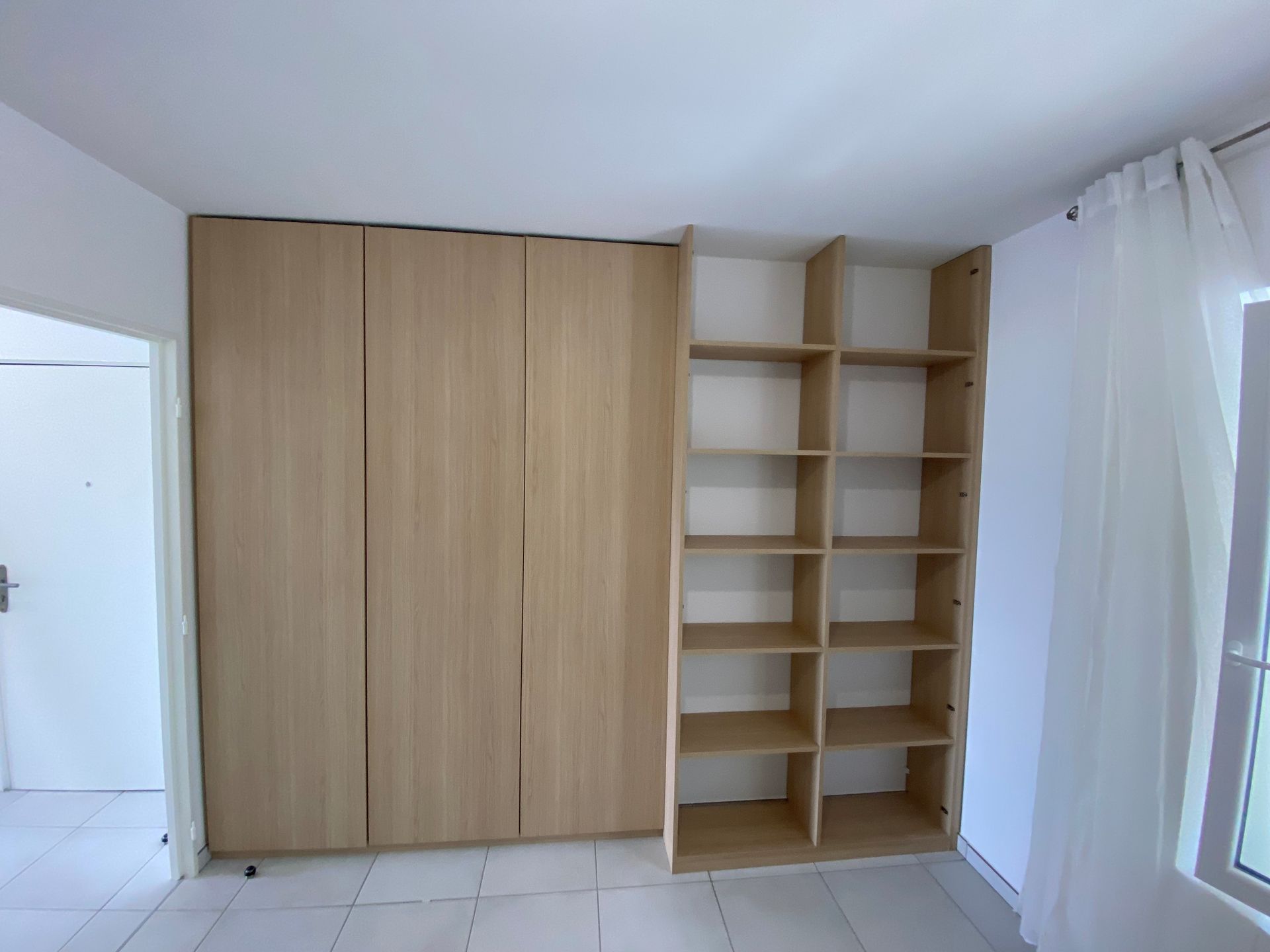Une armoire intégrée en bois avec étagères dans une pièce avec une fenêtre et des murs blancs.