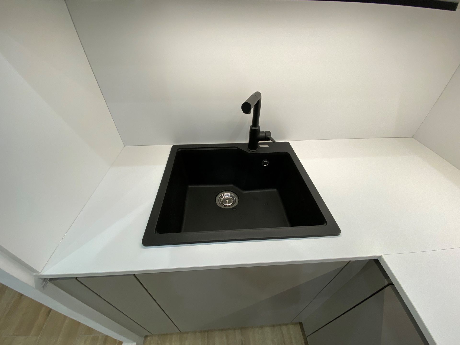 Évier de cuisine noir avec robinet, installé sur un comptoir et des armoires blancs.