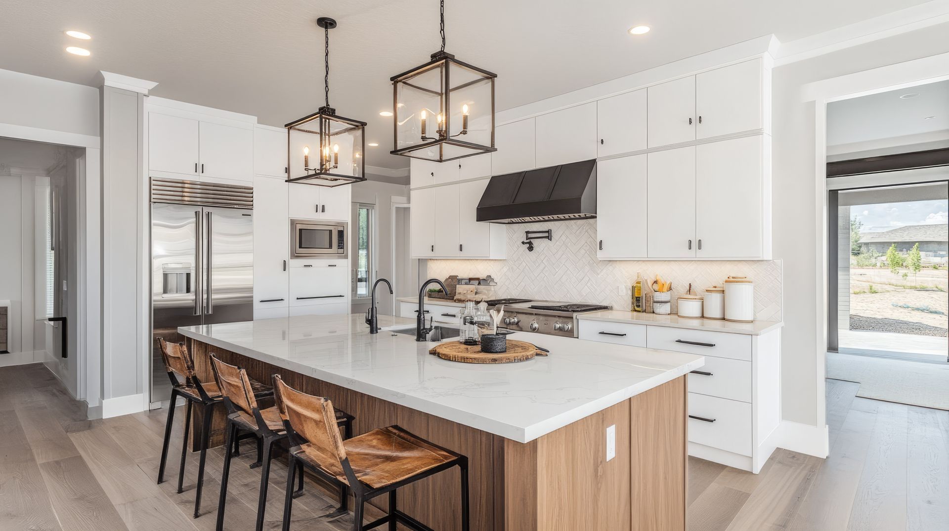Cuisine blanche, lumineuse et moderne avec un îlot central, des suspensions, des tabourets en bois et des appareils électroménagers en acier inoxydable.