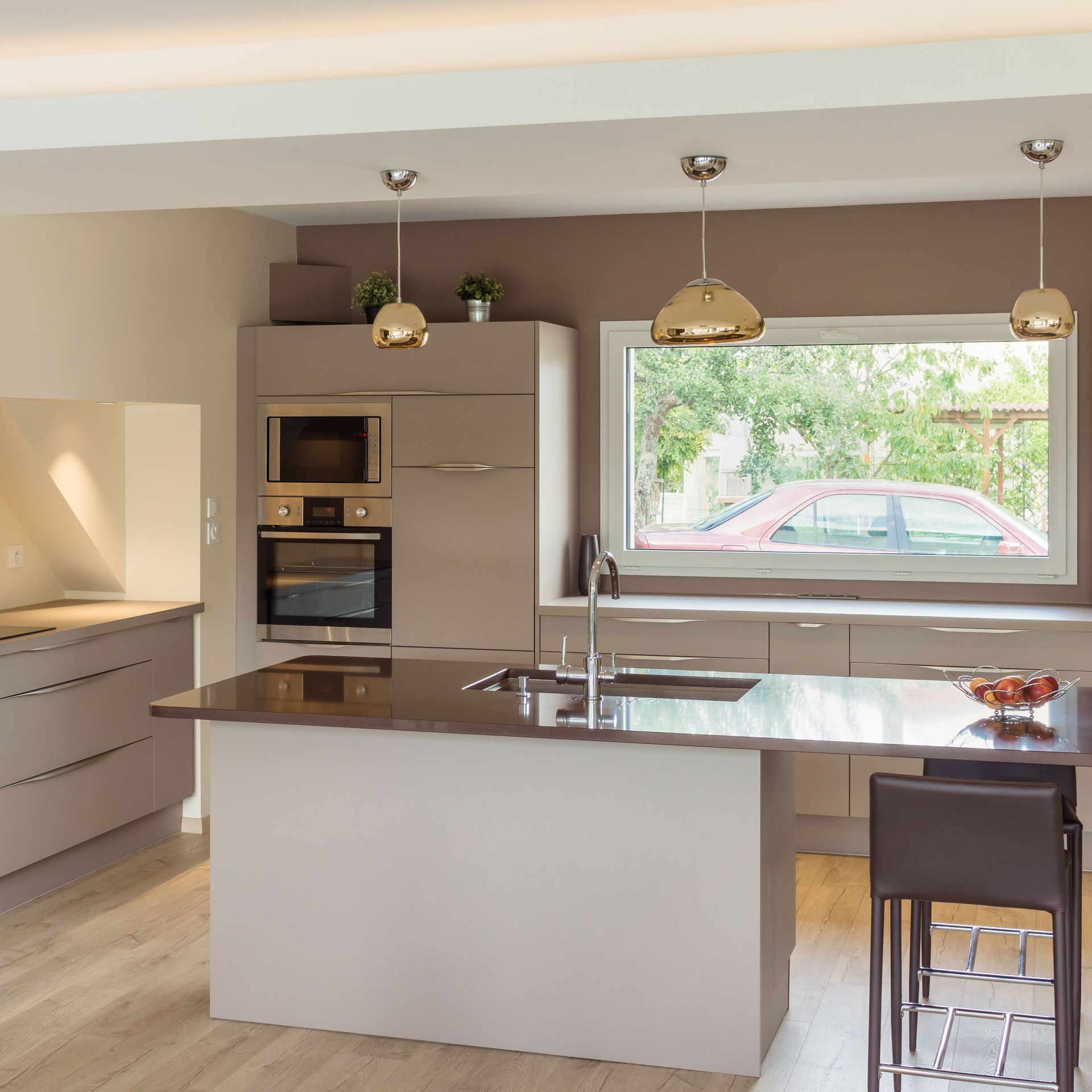 Cuisine moderne avec îlot central, suspensions, four encastré et grande fenêtre au-dessus de l’évier