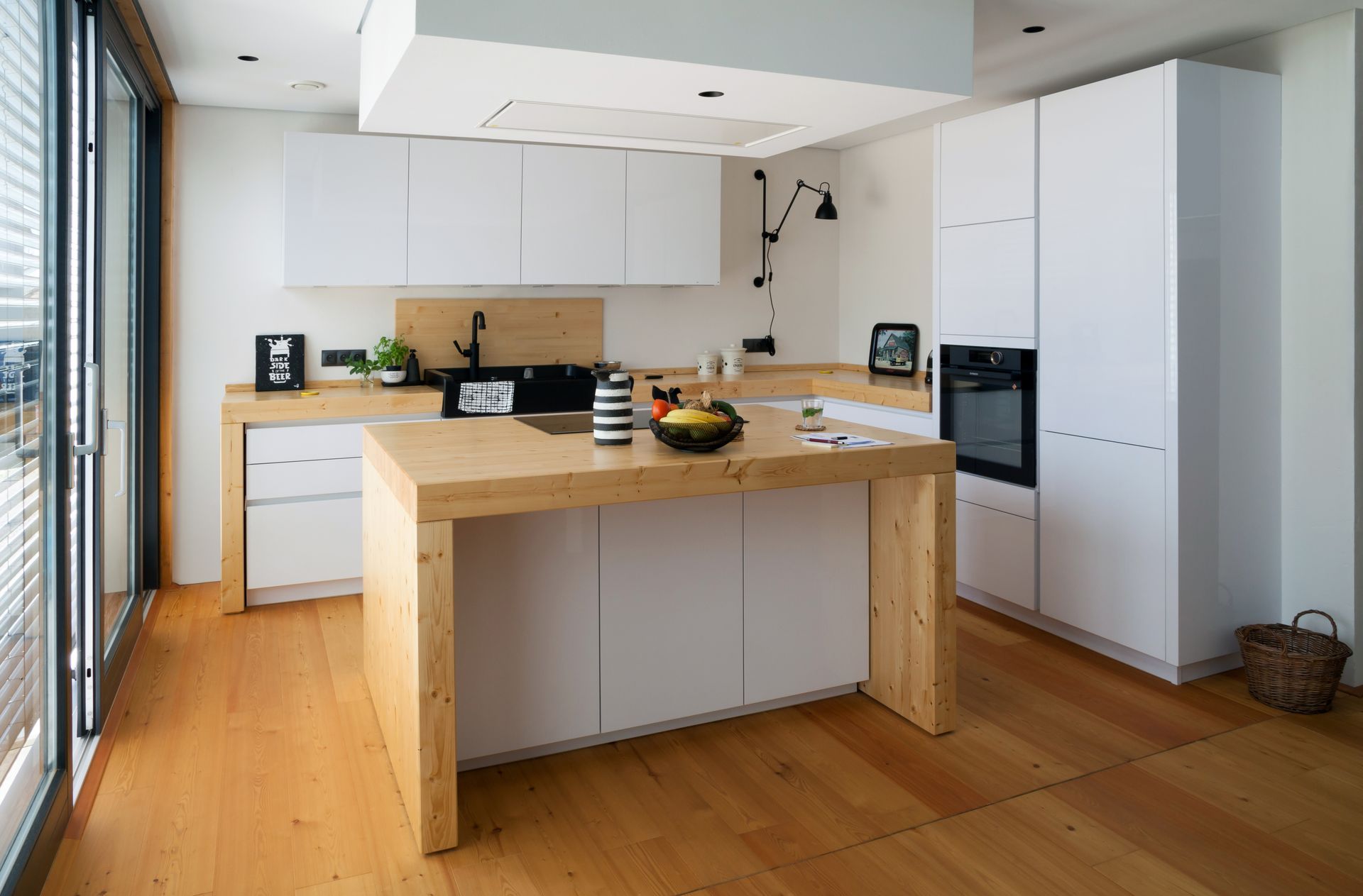 Cuisine moderne et lumineuse avec un parquet en bois, des placards blancs et un grand îlot près d’une baie vitrée coulissante