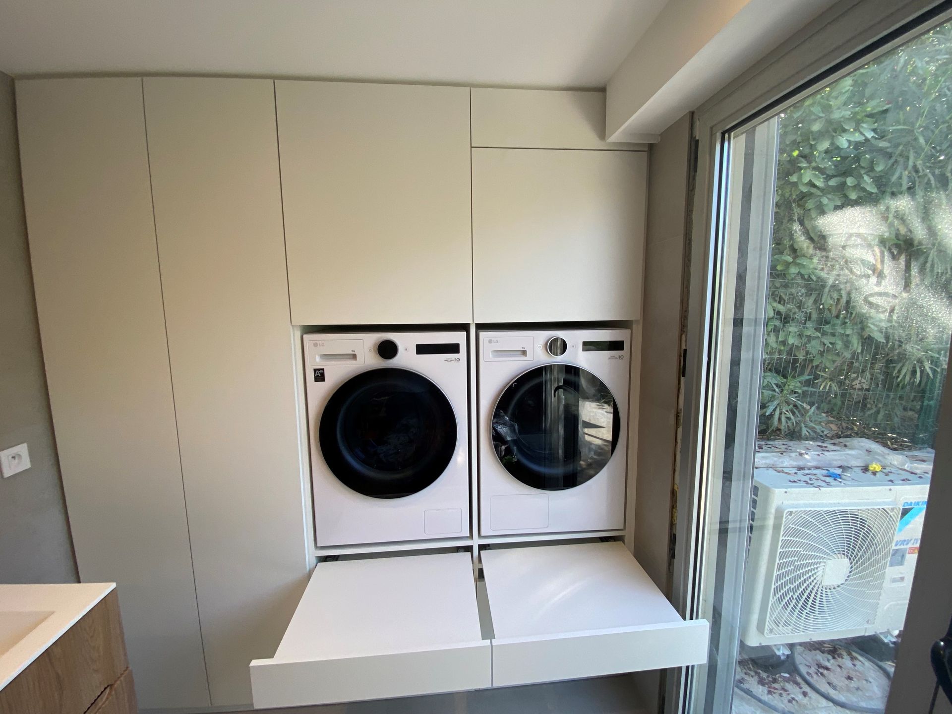 Buanderie avec unités laveuse/sécheuse, armoires de rangement et table pliante; à côté d'une porte coulissante en verre.