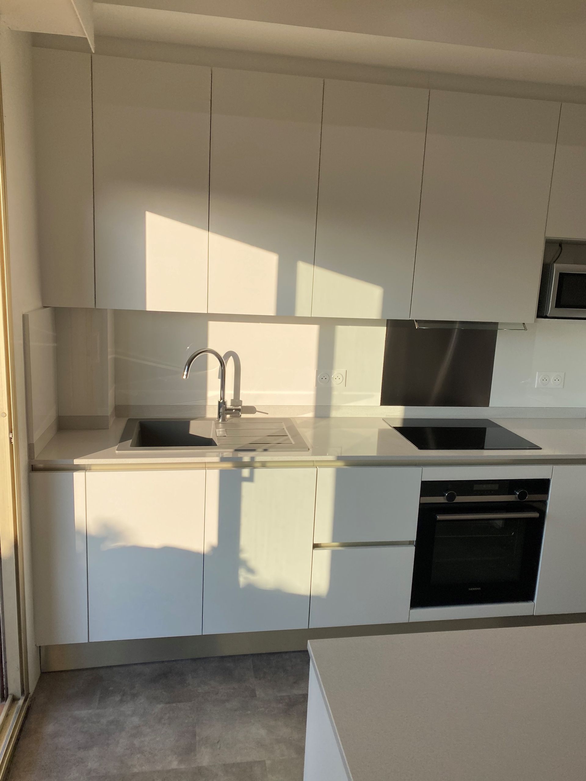 Cuisine moderne blanche avec évier, cuisinière, four et armoires ; lumière du soleil.