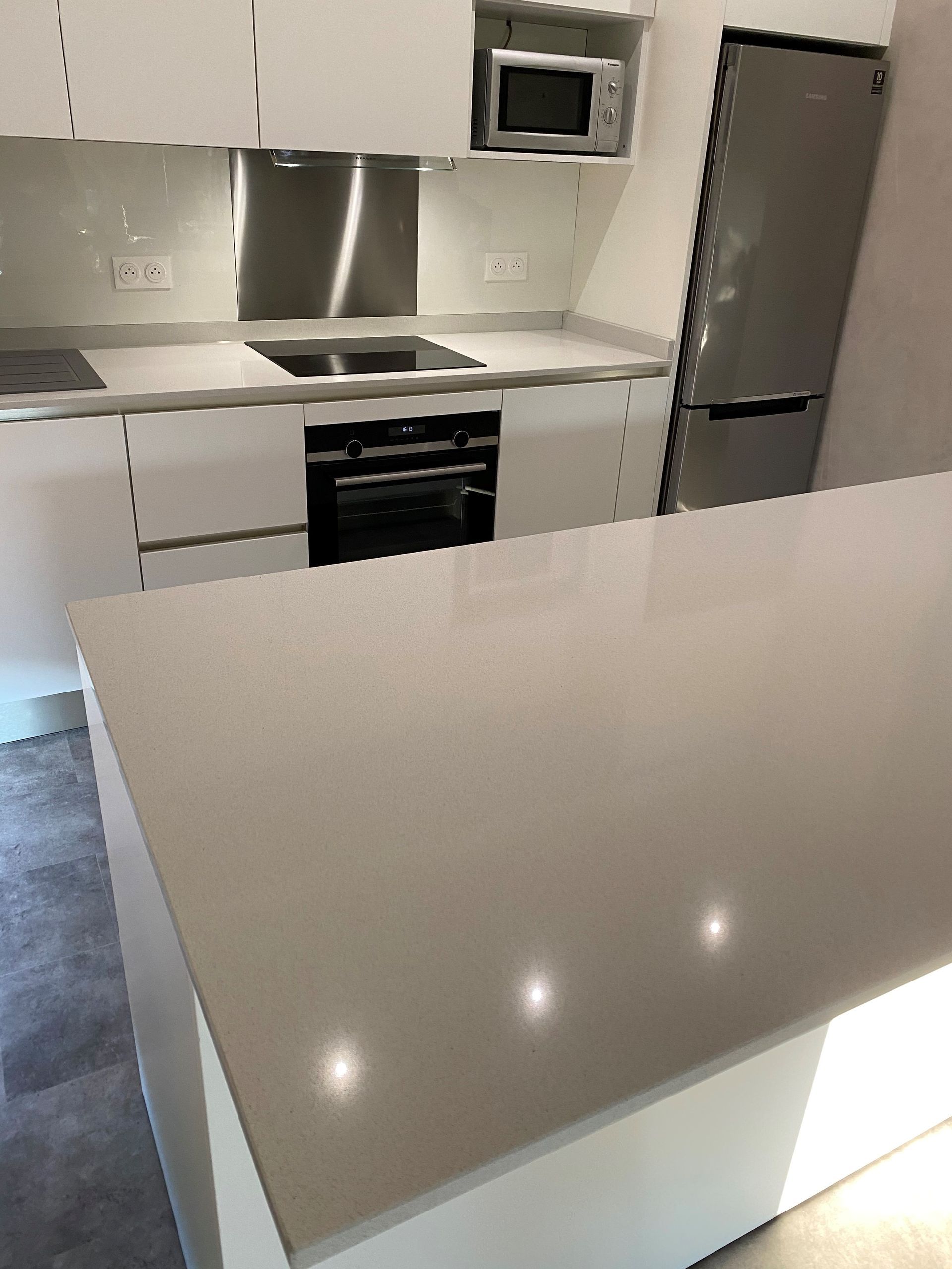 Cuisine blanche moderne avec îlot, électroménagers en acier inoxydable et comptoirs clairs.