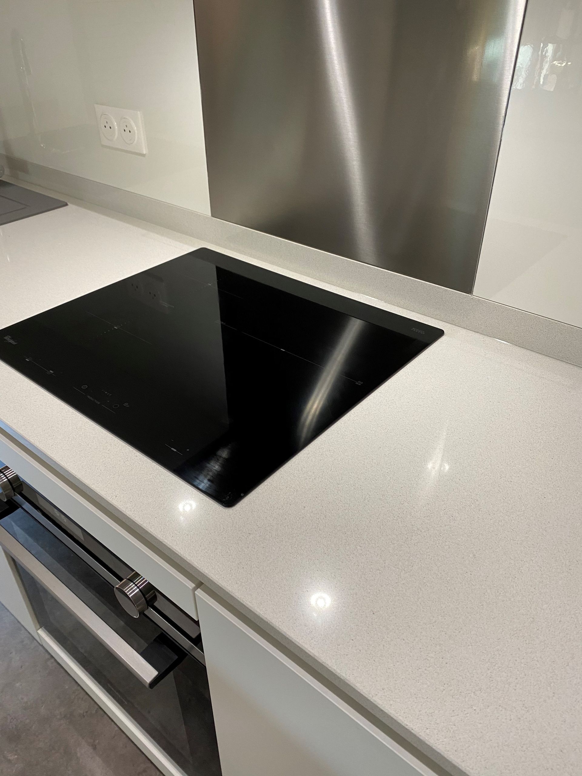 Comptoir de cuisine moderne avec plaque de cuisson noire, dosseret en acier inoxydable et armoires blanches.
