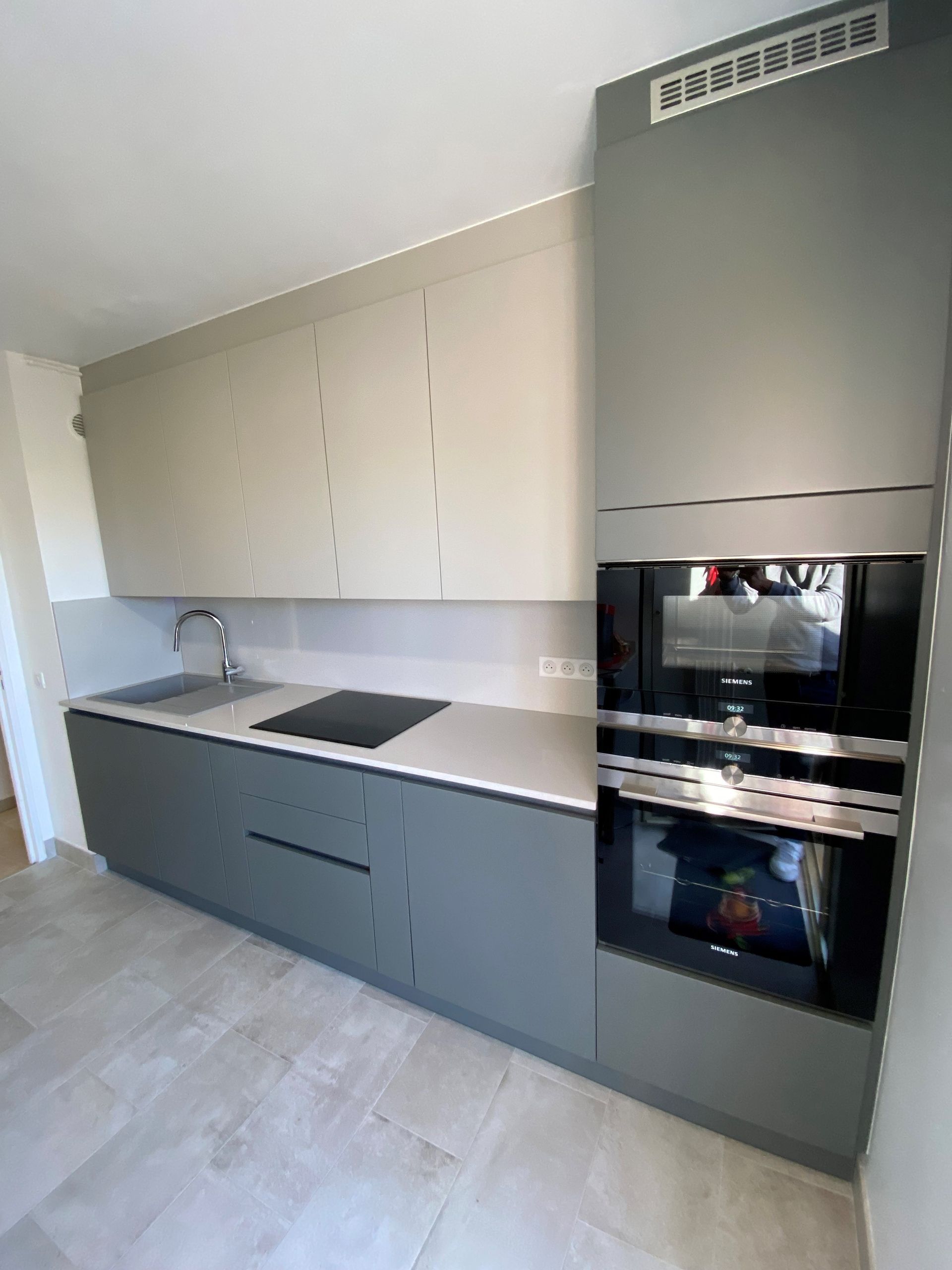 Cuisine moderne avec armoires grises, comptoirs clairs et four et micro-ondes intégrés.