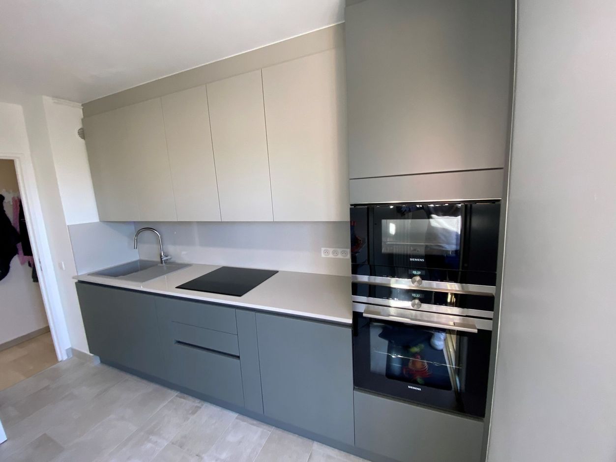 Cuisine grise moderne avec four et micro-ondes intégrés, armoires grises et comptoir clair.