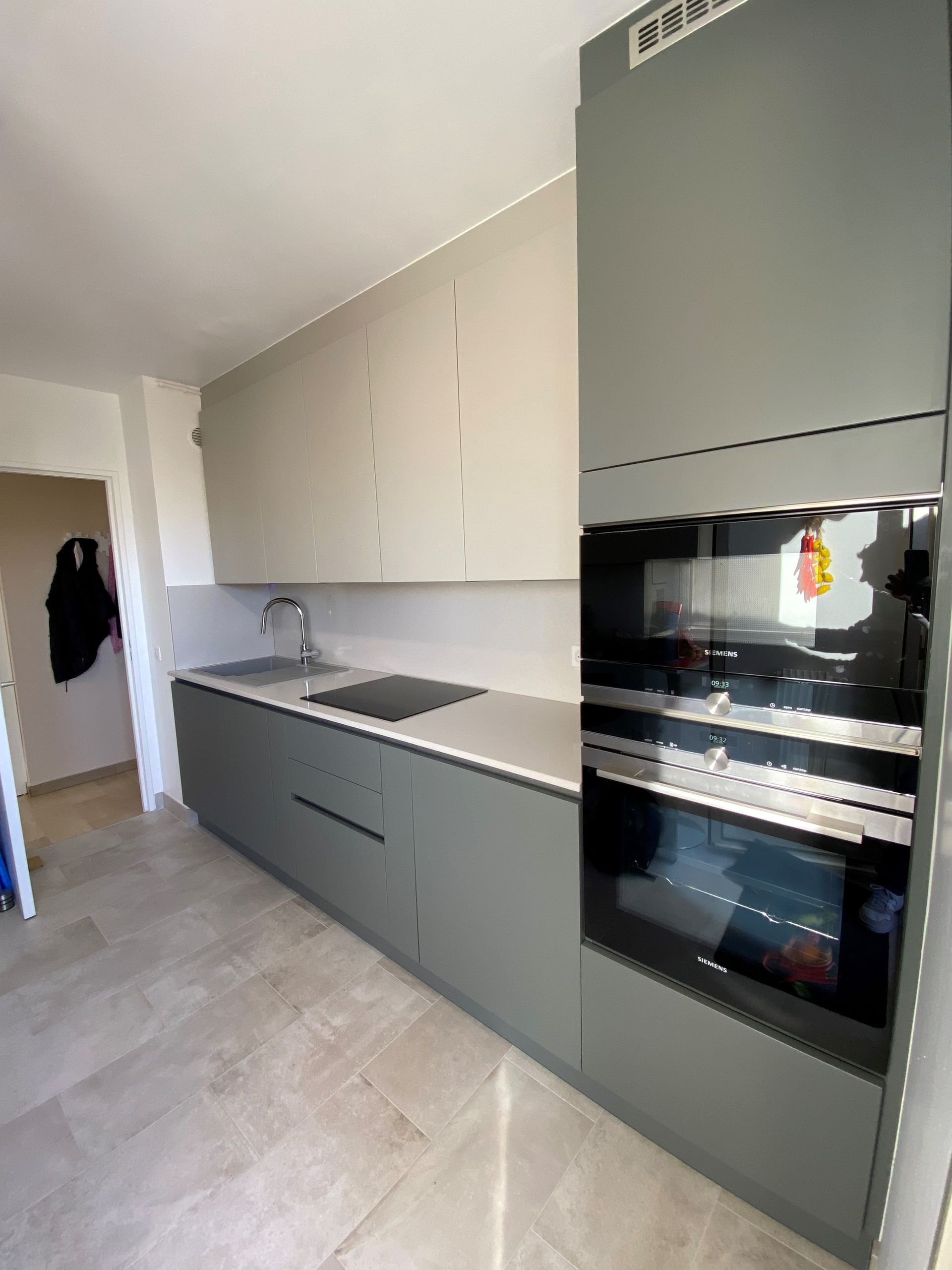 Cuisine grise moderne avec four intégré, évier et armoires contre un mur et un sol clairs.