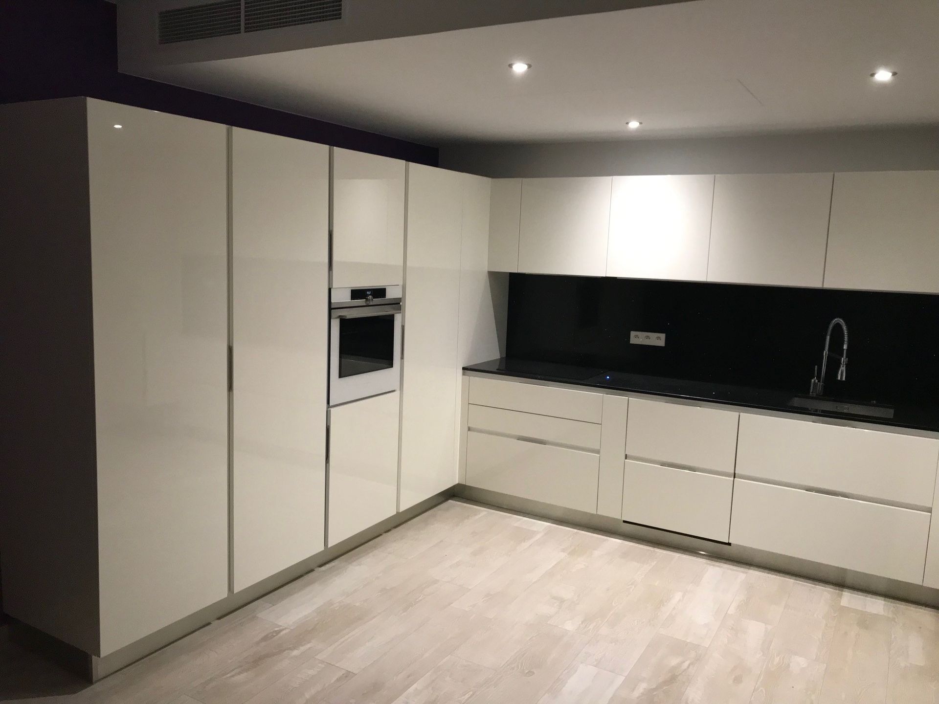 Cuisine blanche moderne avec comptoirs, armoires et four noirs.