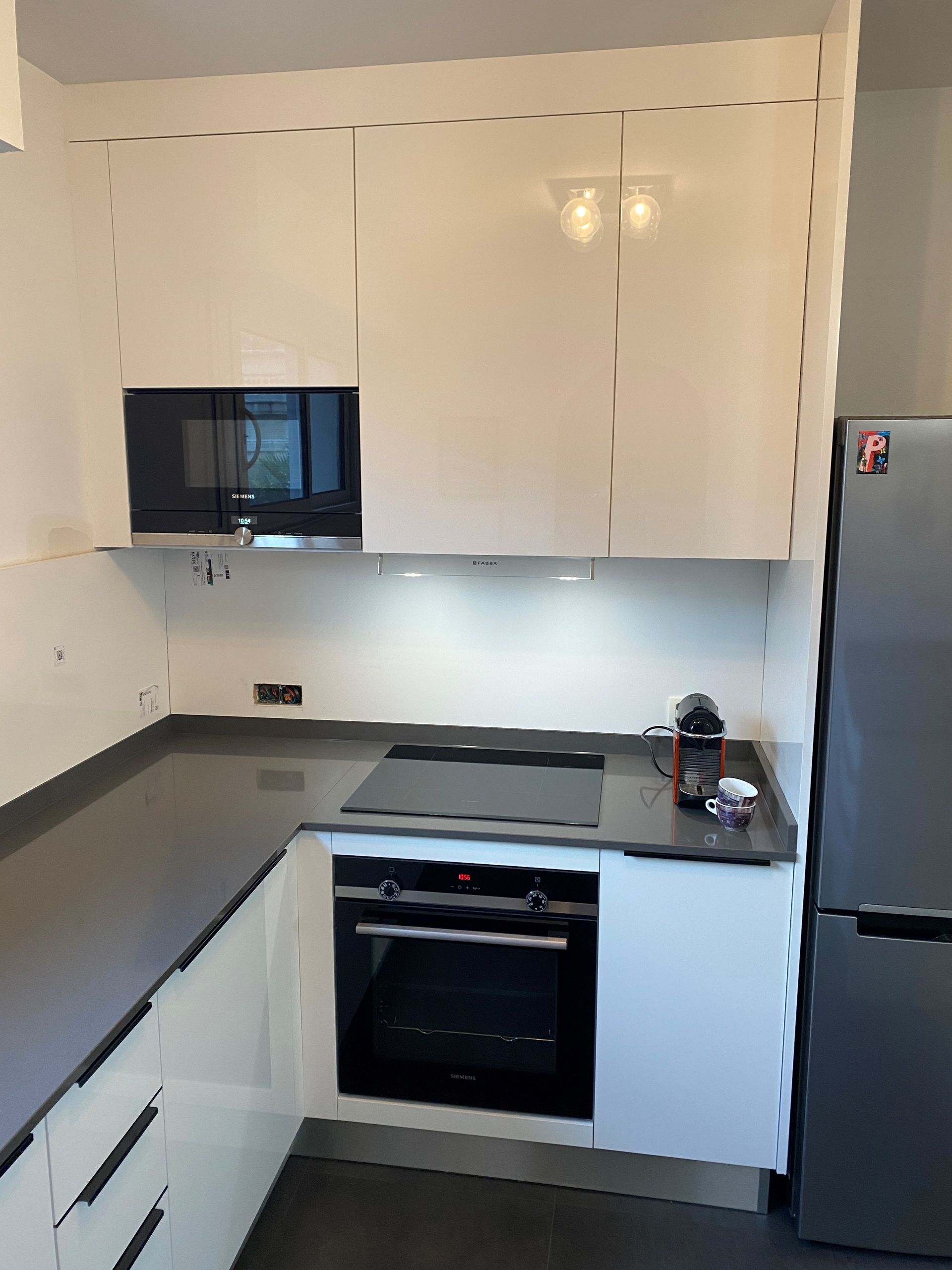 Cuisine blanche moderne avec comptoirs et appareils électroménagers foncés, dont un micro-ondes, un four et un réfrigérateur.