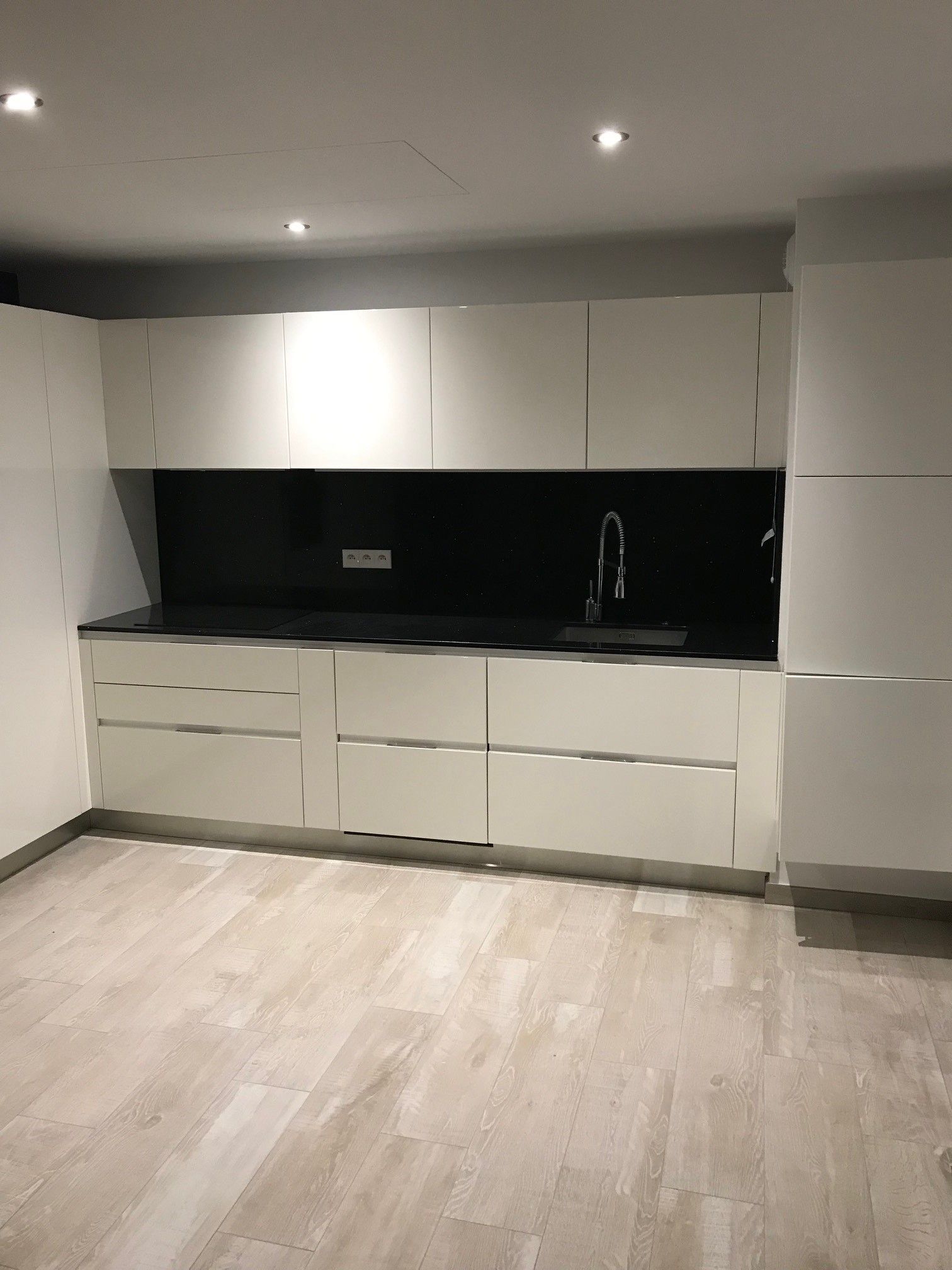 Cuisine moderne blanche avec dosseret noir, armoires et plancher de bois clair.