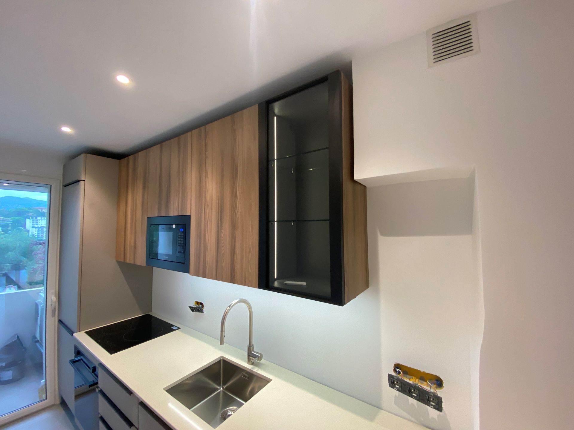 Cuisine moderne avec armoires en bois, évier en acier inoxydable et micro-ondes.