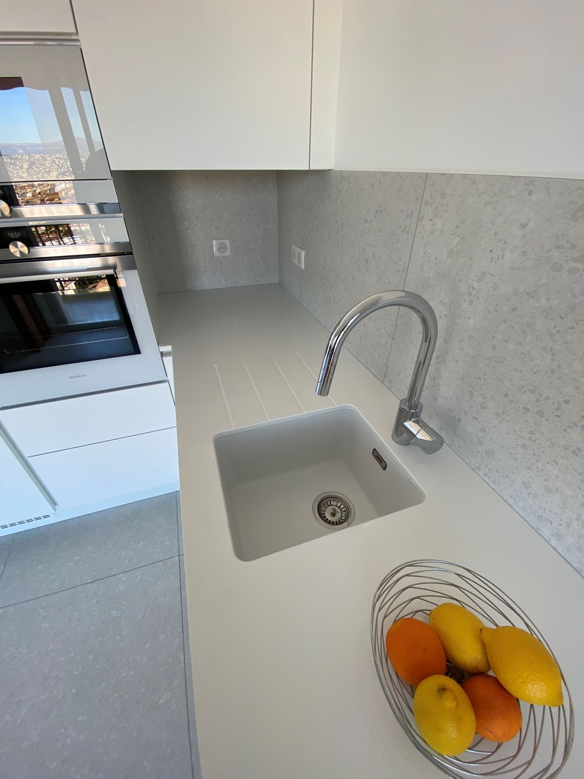 Évier de cuisine blanc avec robinet chromé, dosseret gris, coupe à fruits.