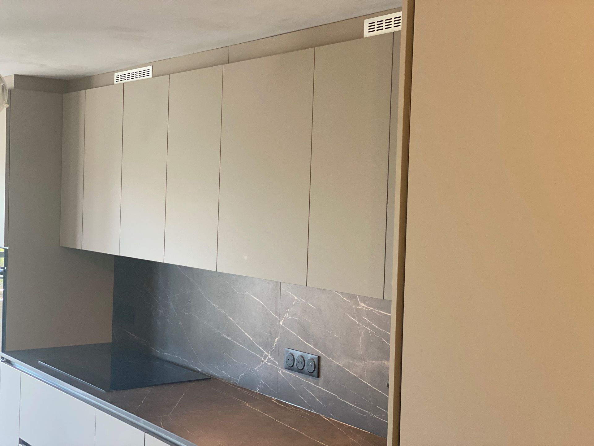Armoires de cuisine beiges au-dessus d'un comptoir avec table de cuisson et dosseret gris, avec mur beige.