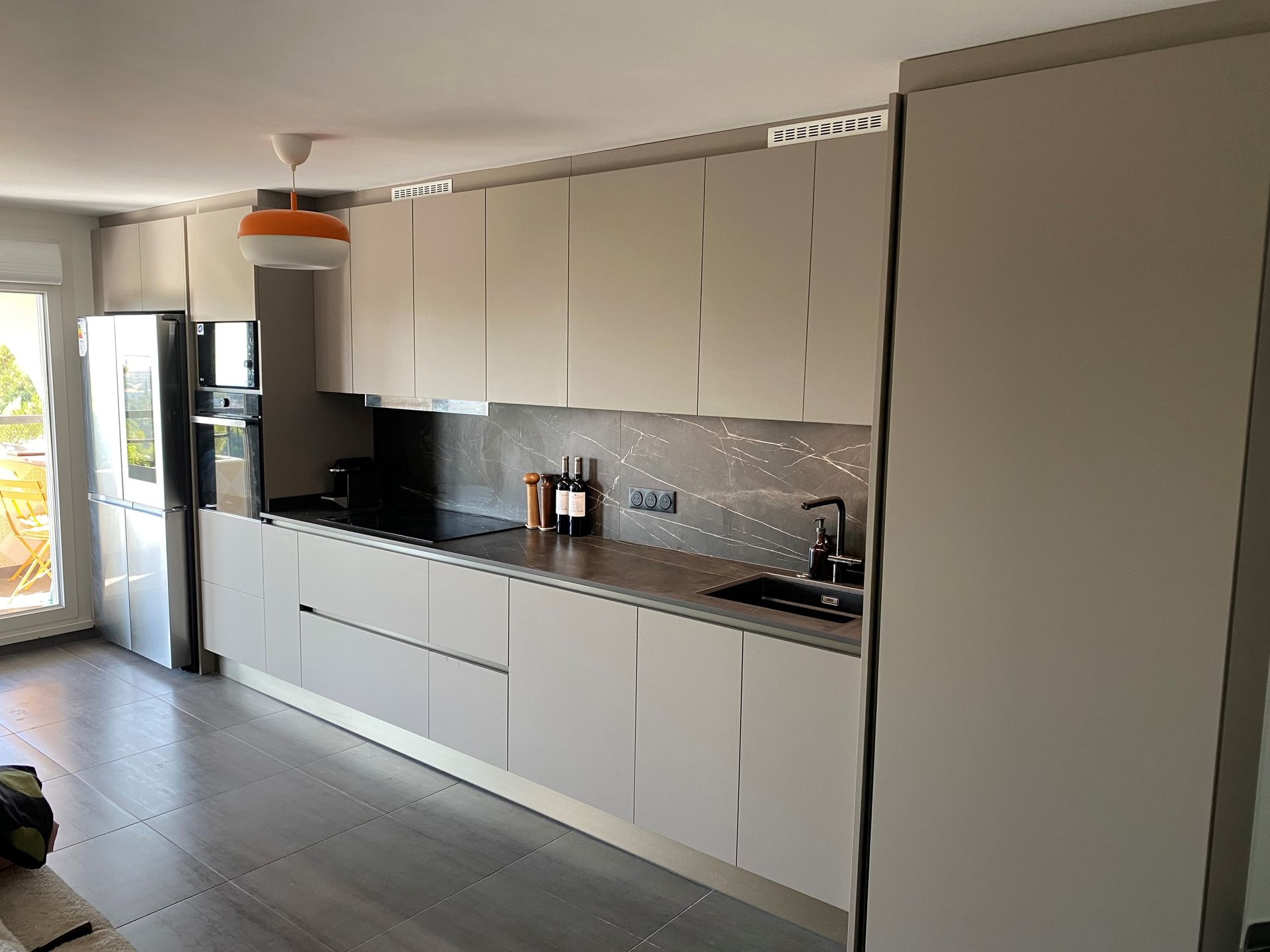 Cuisine moderne avec armoires gris clair, appareils électroménagers en acier inoxydable et comptoir gris.