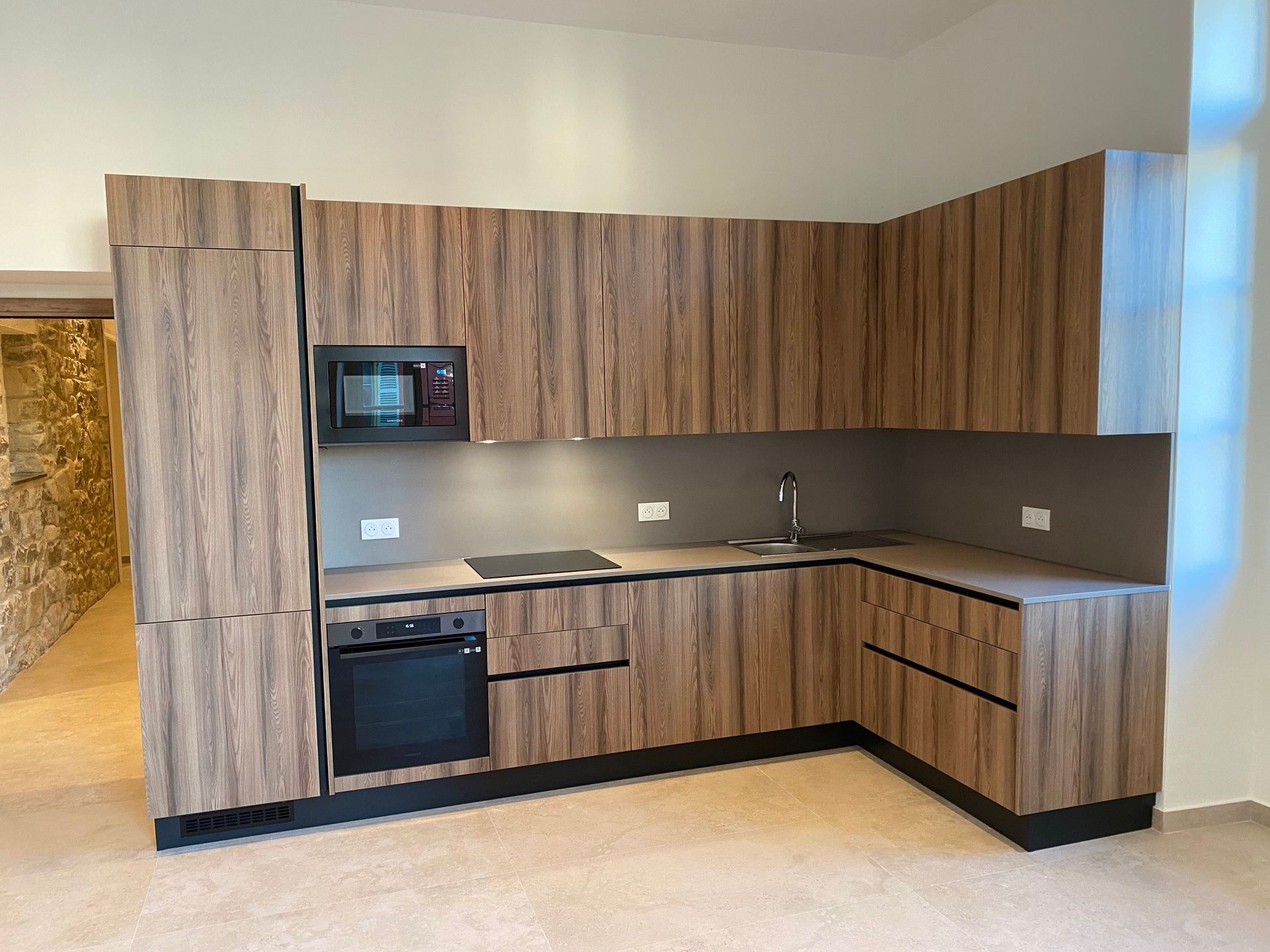 Armoires de cuisine modernes d'aspect bois disposées en coin avec appareils électroménagers intégrés.