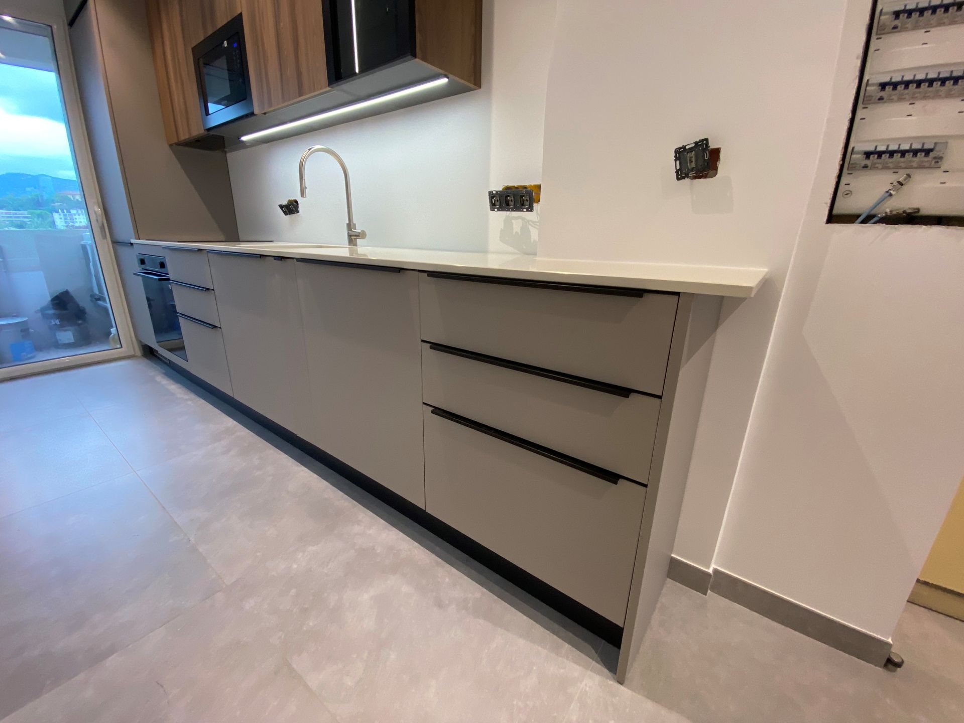 Cuisine moderne avec armoires grises, comptoir clair, robinet en acier inoxydable et appareils électroménagers noirs.