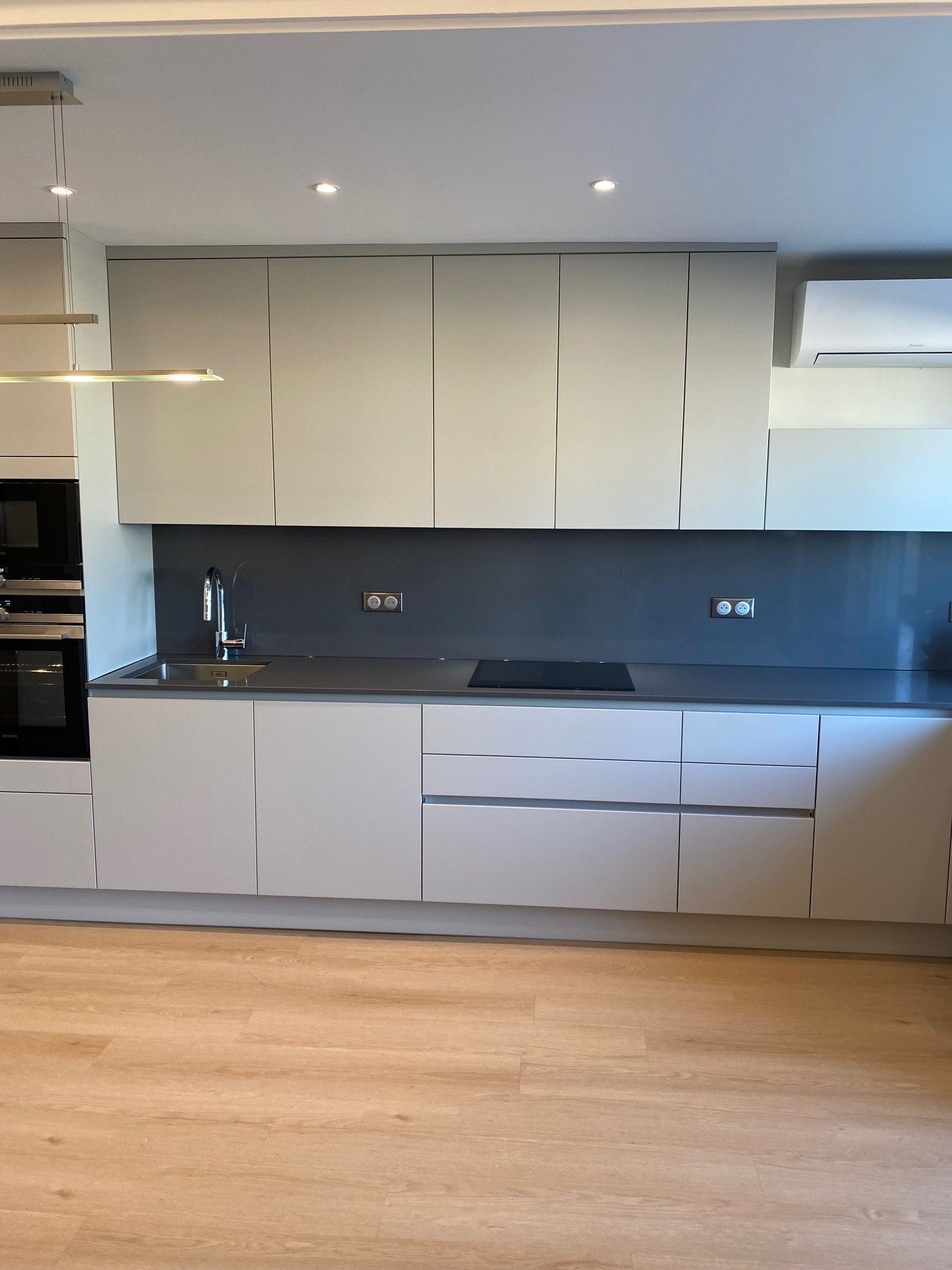 Cuisine moderne avec armoires gris clair, dosseret foncé et plancher de bois.