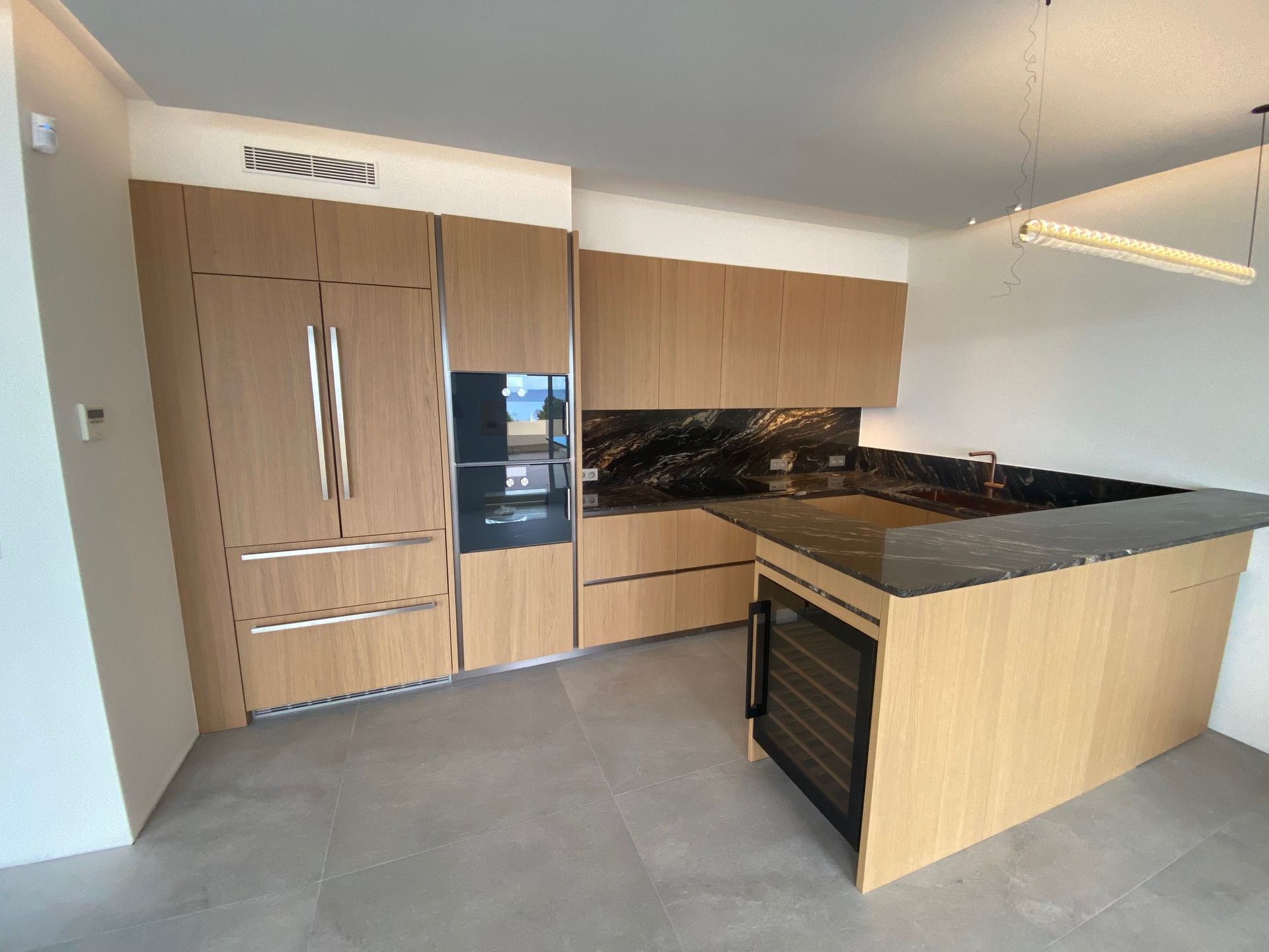 Cuisine moderne avec armoires en bois, comptoirs noirs et réfrigérateur à vin.