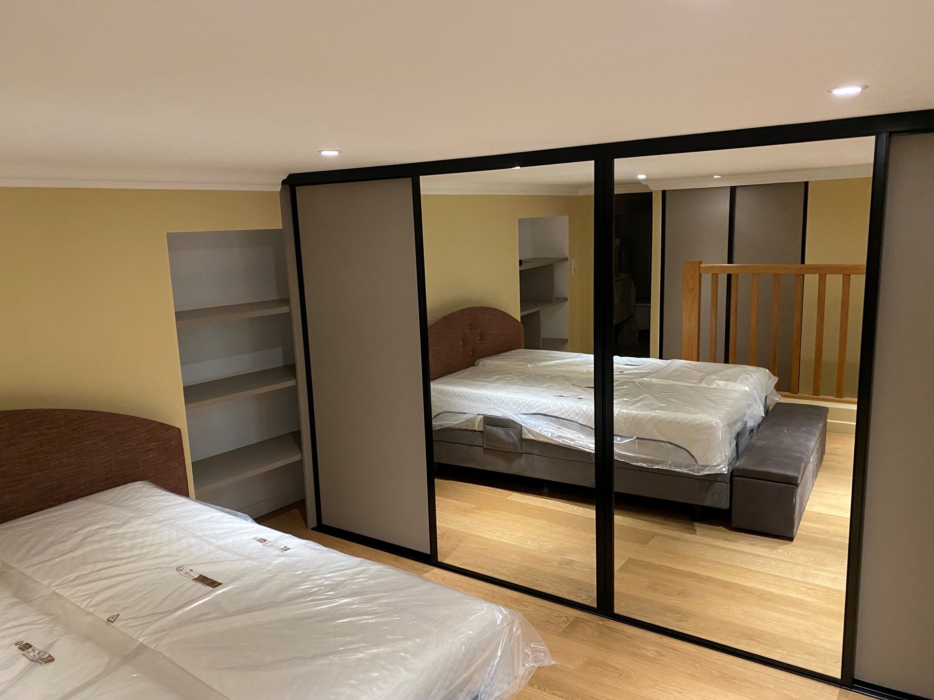 Chambre avec deux lits, portes de placard coulissantes en miroir, étagères intégrées et parquet.