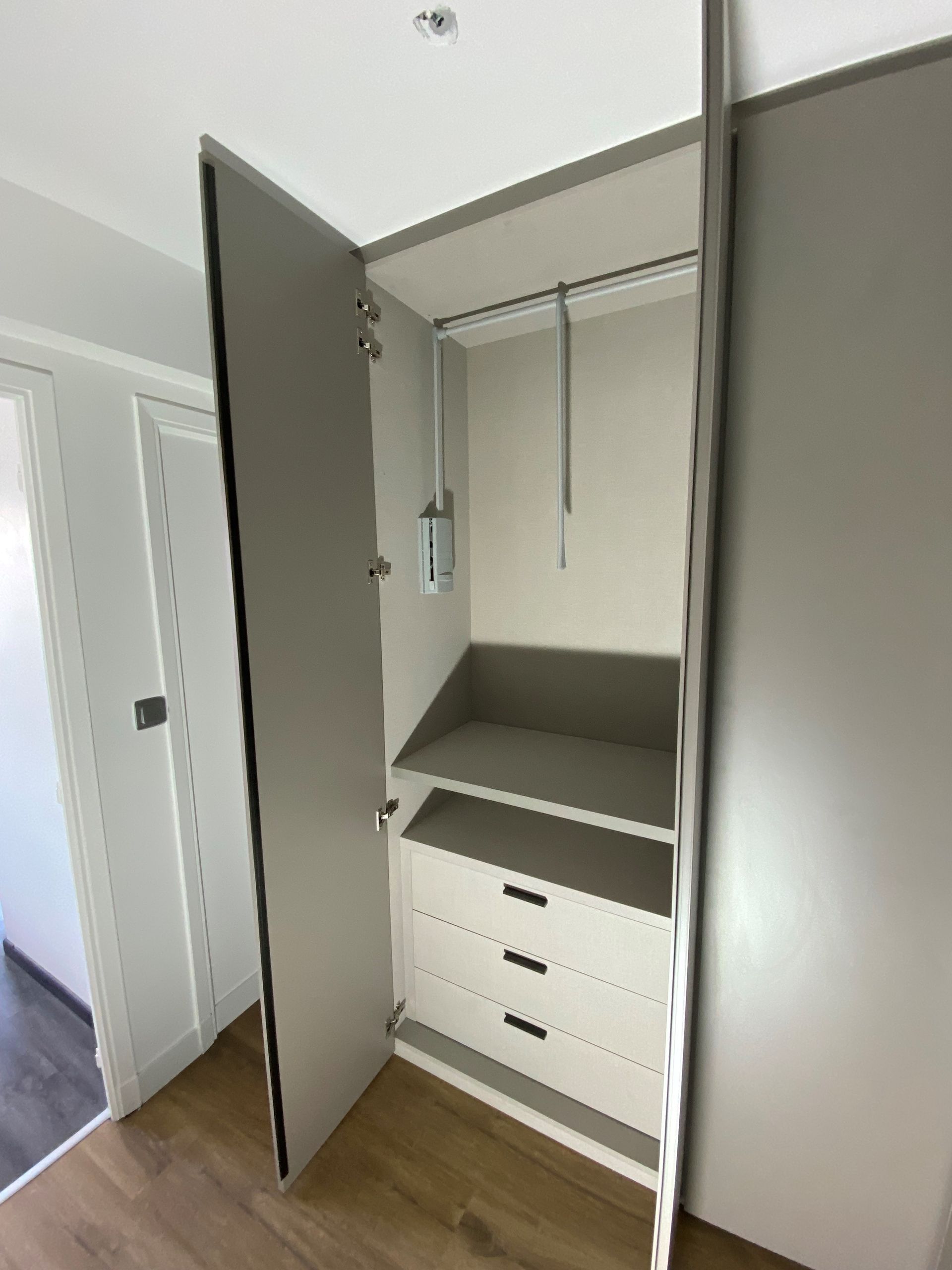 Placard ouvert gris avec tringle à vêtements, étagère et tiroirs.
