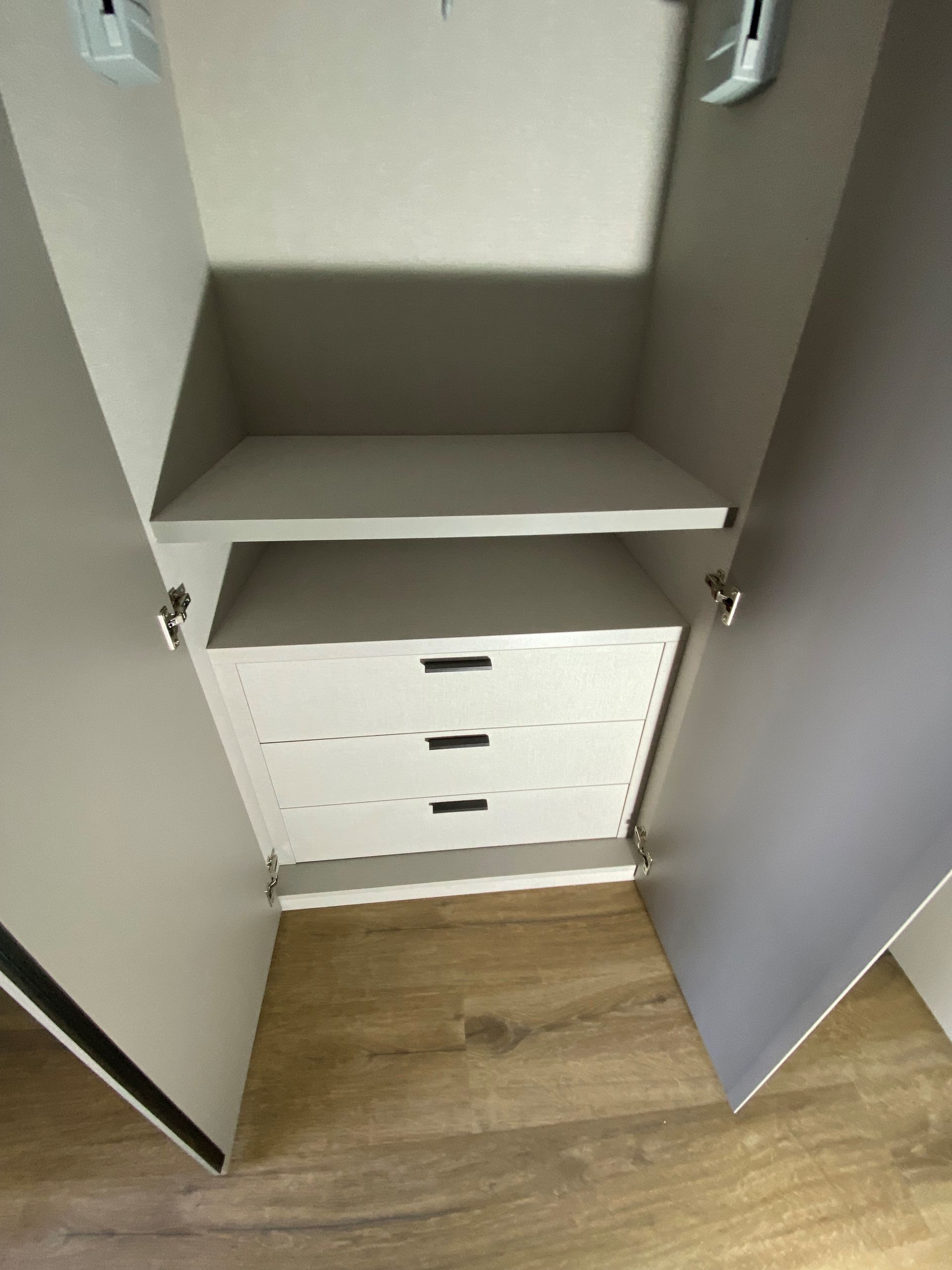 Placard ouvert avec étagère et tiroirs. Intérieur blanc, portes grises, sol imitation bois.