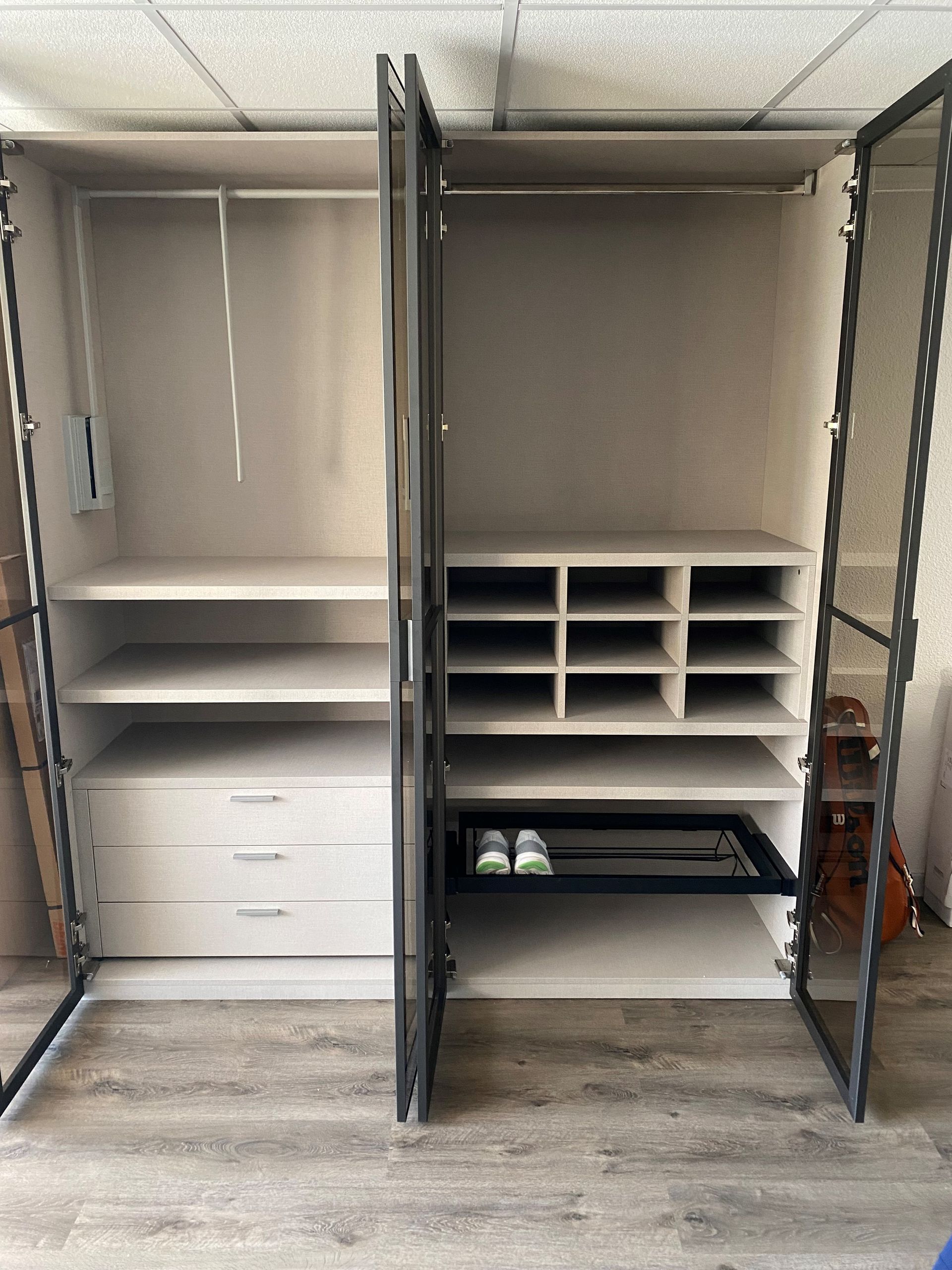 Armoire ouverte avec étagères, tiroirs et rangement à chaussures, avec structure en métal et intérieur beige.