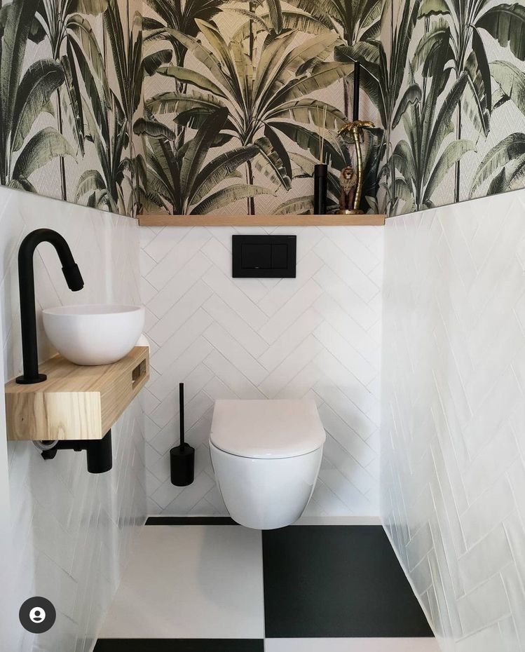 Un baño con inodoro, lavabo y papel pintado tropical.