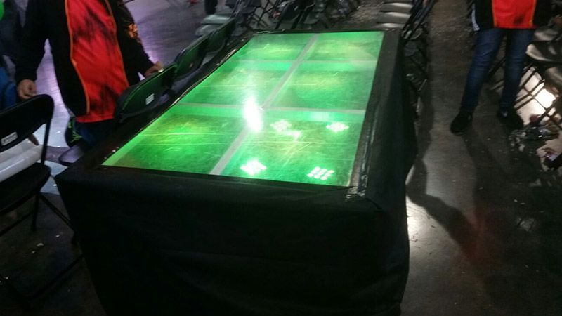 Una mesa con una luz verde y gente de pie alrededor de ella.