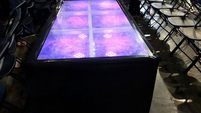 Una mesa con luces violetas está situada delante de una fila de sillas plegables.