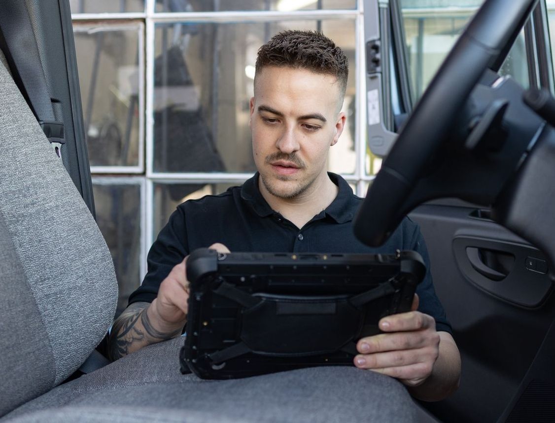 Ein Mann sitzt auf dem Fahrersitz eines Lastwagens und schaut auf ein Tablet.