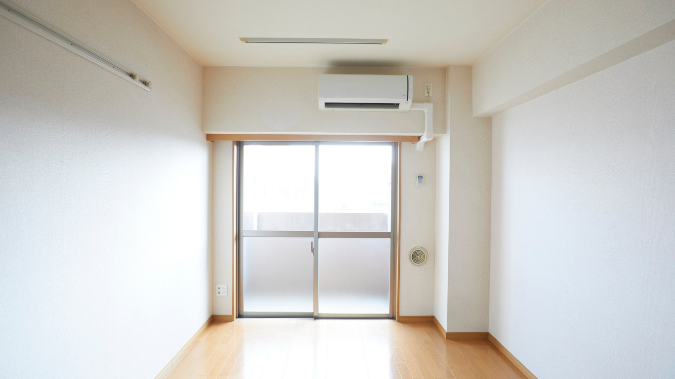 Habitación vacía con puerta corrediza de vidrio al balcón, aire acondicionado en la pared, piso de madera.