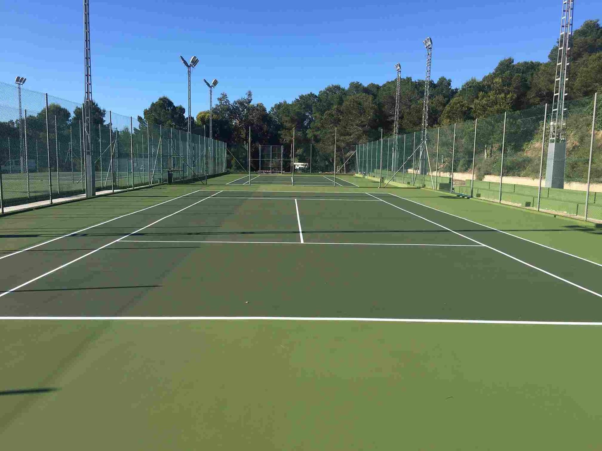 Una cancha de tenis con una valla alrededor en un día soleado.