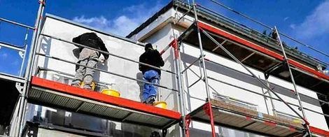 Dos hombres están de pie sobre un andamio al costado de un edificio.