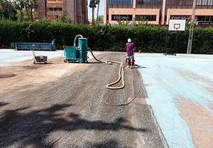 Un hombre está pintando una cancha de baloncesto con una aspiradora.