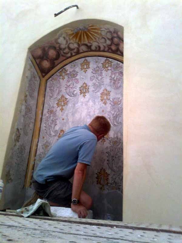 Un hombre está arrodillado frente a una pared con un patrón en ella.