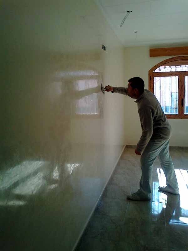 Un hombre está de pie en una habitación pintando una pared.
