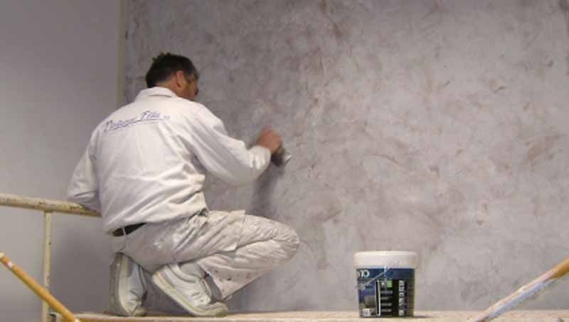 Un hombre está arrodillado en un andamio pintando una pared.