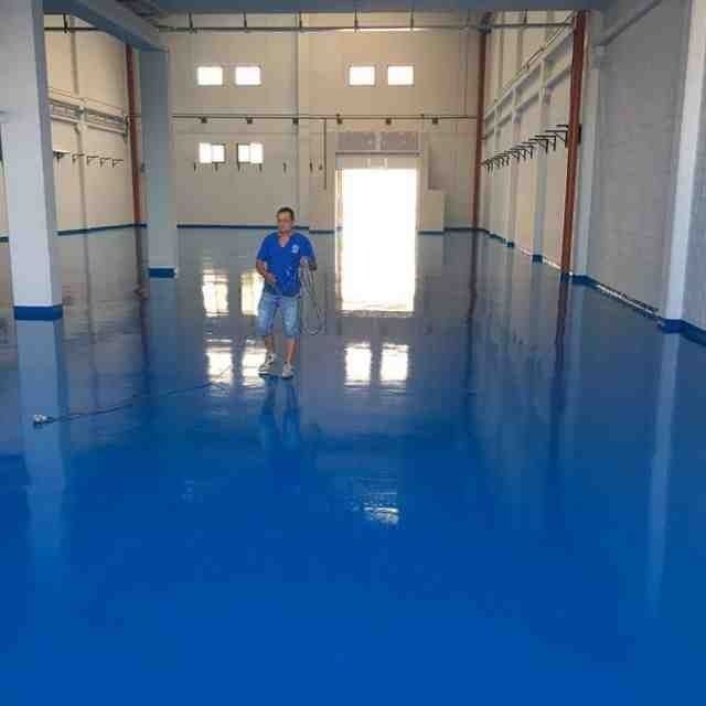 Un hombre está de pie en una habitación grande con un piso azul.