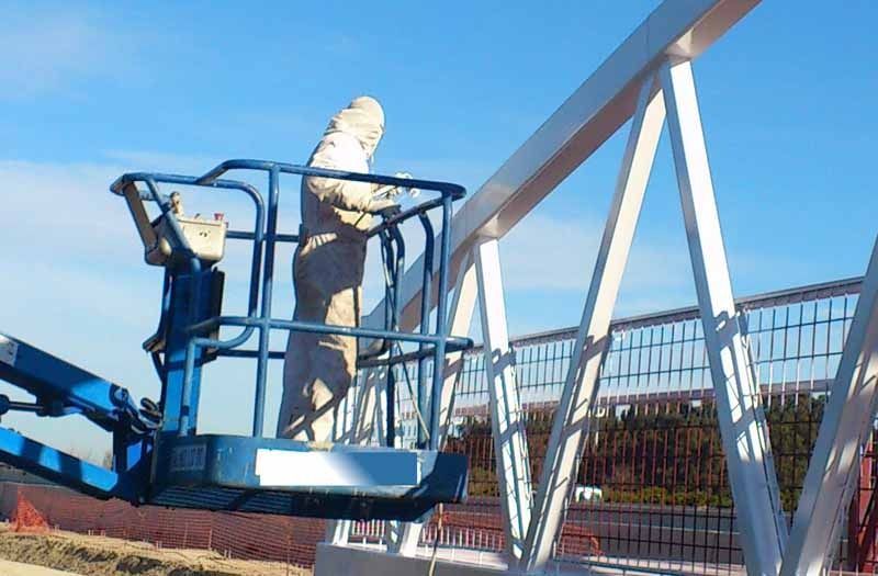 Un hombre en una jaula está pintando una estructura de metal.